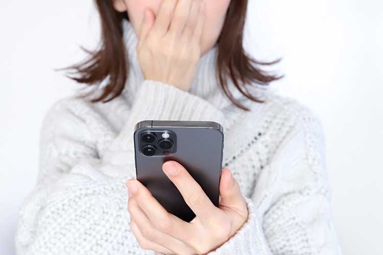 iPhoneを見ながら口元を押さえている女性