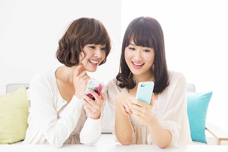 スマホを片手に笑顔で画面を操作する二人の若い女性